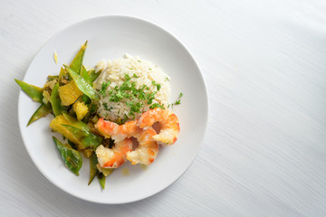 fried tiger prawn shrimps with vegetables from sugar peas and oranges, served with rice on a white plate, copy space, high angle view from above,  selected focus