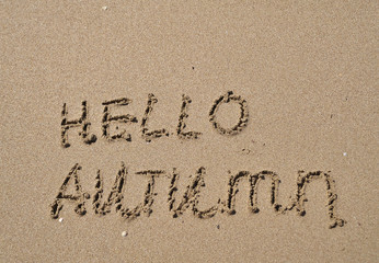 The words Hello autumn written on sand.