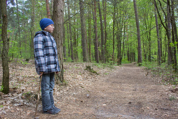 boy stands in the forest,boy standing in the woods near the forest road, side view of the boy in the forest