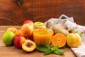 Fruits lie on a wooden table. In the center is a glass of fruit juice.