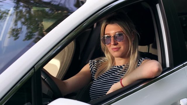 Portrait of a young girl in sunglasses driving a car on a sunny summer day.