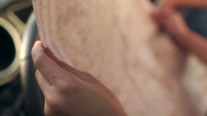 Close-up of the girl studying the map sitting in the car behind the wheel. A woman looks at the route on the city map. Summer travel. Slow motion.