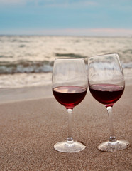 Wineglass with red wine on the beach at sunset. Romantic concept.