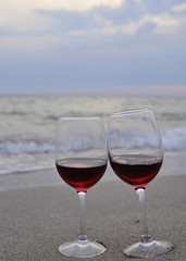 Glasses with red wine on the beach at sunset. Romantic concept.