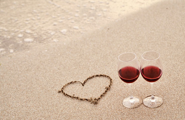 Glasses with red wine on the beach at sunset. Romantic concept.