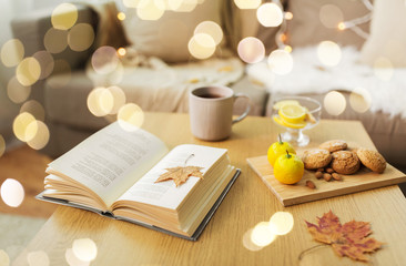 Obraz na płótnie Canvas hygge and cozy home concept - book, autumn leaves, cup of tea with lemon, almond nuts and oatmeal cookies on table