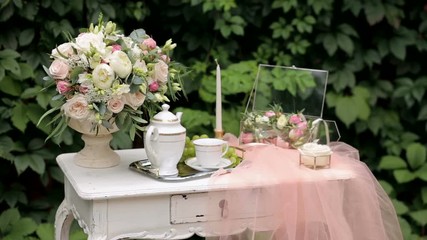 Wedding decor. Vintage table with bouquets of flowers, tea set and transparent veil on the background of green leaves. Morning for bride.