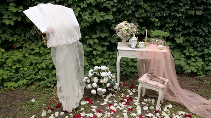 Wedding decor. Vintage table with bouquets of flowers, tea set and transparent veil on the background of green leaves. Morning for bride.