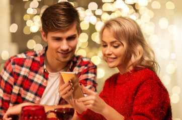 Obraz na płótnie Canvas holidays, technology and celebration concept - happy couple having christmas dinner at home and using smartphone