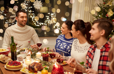 holidays and celebration concept - happy friends having christmas dinner at home and eating