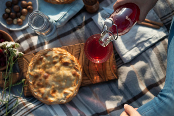 Woman pouring drink into glass sitting on the blanket