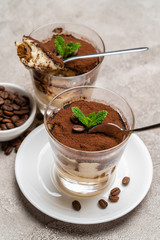 Portion of Classic tiramisu dessert in a glass cup on concrete background