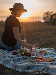 Pretty young woman enjoying picnic in autumn field at sunset