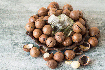 Ripe macadamia nuts and a glass bottle with natural oil on a round brown dish. Source of natural vitamins and minerals. Selective focus.