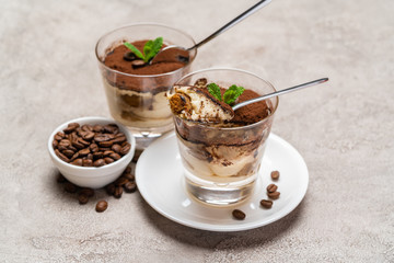 Portion of Classic tiramisu dessert in a glass cup on concrete background