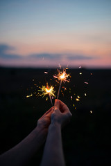 Hands holding sparkling fireworks to the sky at twilight