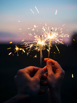 Couple holding sparkling fireworks to the sky at twilight