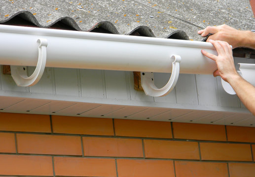 Contractor installing plastic roof gutter. Plastic Guttering, Rain Guttering & Drainage by Handyman hands.