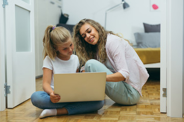 mother and daughter sitting floor and using laptop computer at home