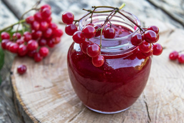 Viburnum fruit jam in a glass jar on a wooden table near the ripe red viburnum berries. Source of natural vitamins. Used in folk medicine.
