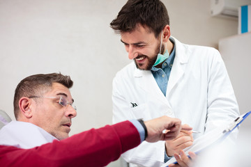 Serious mature man consulting with his doctor in medical clinic. Happy young doctor examining male patient in his office, filling out forms on a clipboard