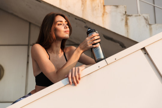 Image of brunette woman standing on stairs outdoors with water bottle