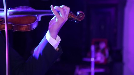 Musician playing violin. Close-up male musician playing violin on dark background with colorful lights.