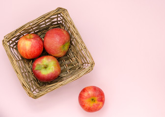 Ripe juicy apples of new crop. Group of red apples in a small wicker basket isolated on pink background with copy space. Symbol of healthy lifestyle. Fruits rich in vitamins, iron. Organic food.