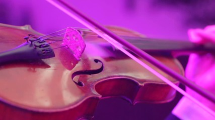 Musician playing violin. Close-up male musician playing violin on dark background with colorful lights.