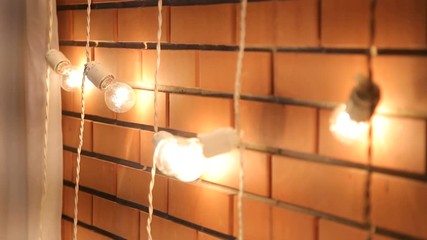 Brick wall with a garland of light bulbs. Lights Decorations for Celebratory design. Light bulbs near the brick wall. Incandescent bulbs on brick wall background in loft style.