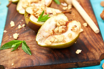 Tasty roast pears with honey and walnuts on wooden board on blue background table.