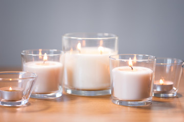 decoration, hygge and cosiness concept - burning white fragrance candles on wooden table