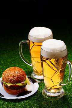 Two glasses of beer and hamburger on green grass.