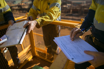 Miner supervisor checking reviewing document before issued sigh of working at height permit JSA risk assessment on site prior to performing high risk work on construction mine site, Perth, Australia  - obrazy, fototapety, plakaty