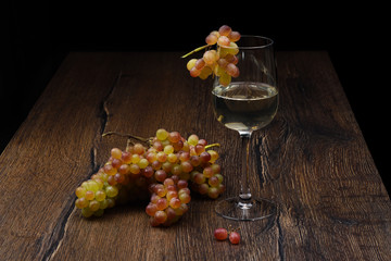 Glass of white wine and a bunch of grapes on wooden table.