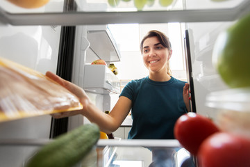healthy eating, food and diet concept - happy woman taking meat from fridge at home kitchen