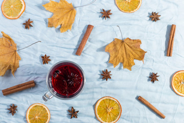 A cup of mulled wine with spices, dry leaves and oranges on the table. Autumn mood, method to keep warm in cold, copy space, morning light, flat lay.