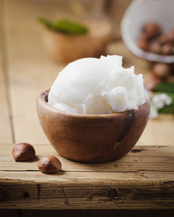 Shea butter in wooden bowl with nuts on old rustic table. Free text space.
