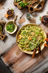 overhead shot of tasty homemade italian pasta with grilled shrimps, pesto sauce, parmesan cheese, fresh basil in ceramic bowl on wooden rustic table