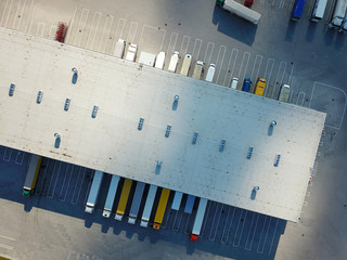Aerial view of goods warehouse. Logistics center in industrial city zone from above. Aerial view of trucks loading at logistic center. View from drone.