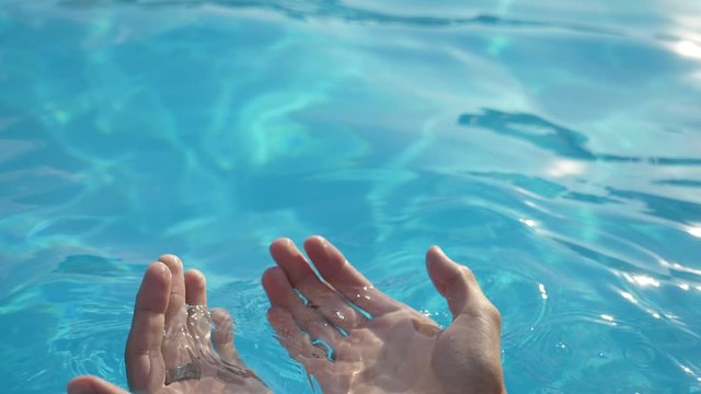 Male hands taking blue water in handfuls and raising it in celeste pool in slo-mo  