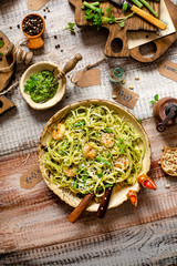 overhead shot of tasty homemade italian pasta with grilled shrimps, pesto sauce, parmesan cheese, fresh basil in ceramic bowl on wooden rustic table
