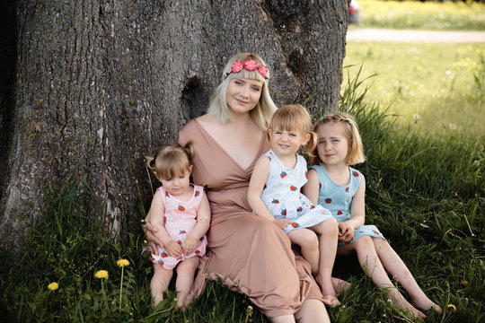 Mother having quality funny playing time with her baby girls at a park blowing dandelion - Young blonde hippie - Daughters wear similar dresses with strawberry print - Family values
