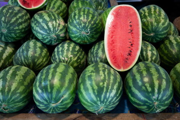 heap of green watermelon and piece of red watermelon fruits on wooden table in market .