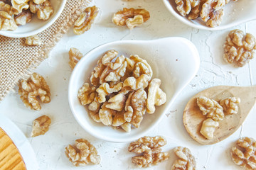 Natural brown walnuts in bowls on a white wooden table of a rustic kitchen. Sackcloth and wood spoon with empty copy space for Editor's text.