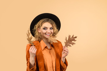 Autumn girl in black hat. Happy woman with autumn leaves in orange jacket. Woman autumn fashion. Fashionable woman with autumn leaves in hand. Fall. October. Beautiful model girl with autumnal leaves.