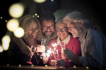 group of two seniors and two adults together having fun with sparlers the new year to celebrate -...
