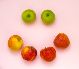 Ripe juicy apples of new crop. Group of colorful apples in a shape of smile isolated on pink background. Symbol of healthy lifestyle. Fruits rich in vitamins, iron. Harvest festival, organic food. 