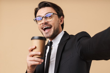 Image of happy businessman holding coffee cup while taking selfie photo