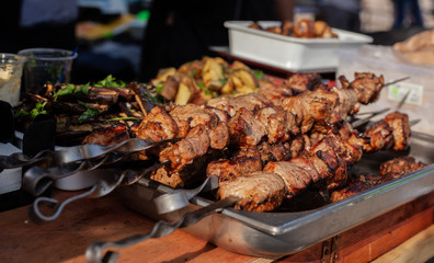 Roasted meat on a skew is on the table next to fried potatoes and vegetables in the open air